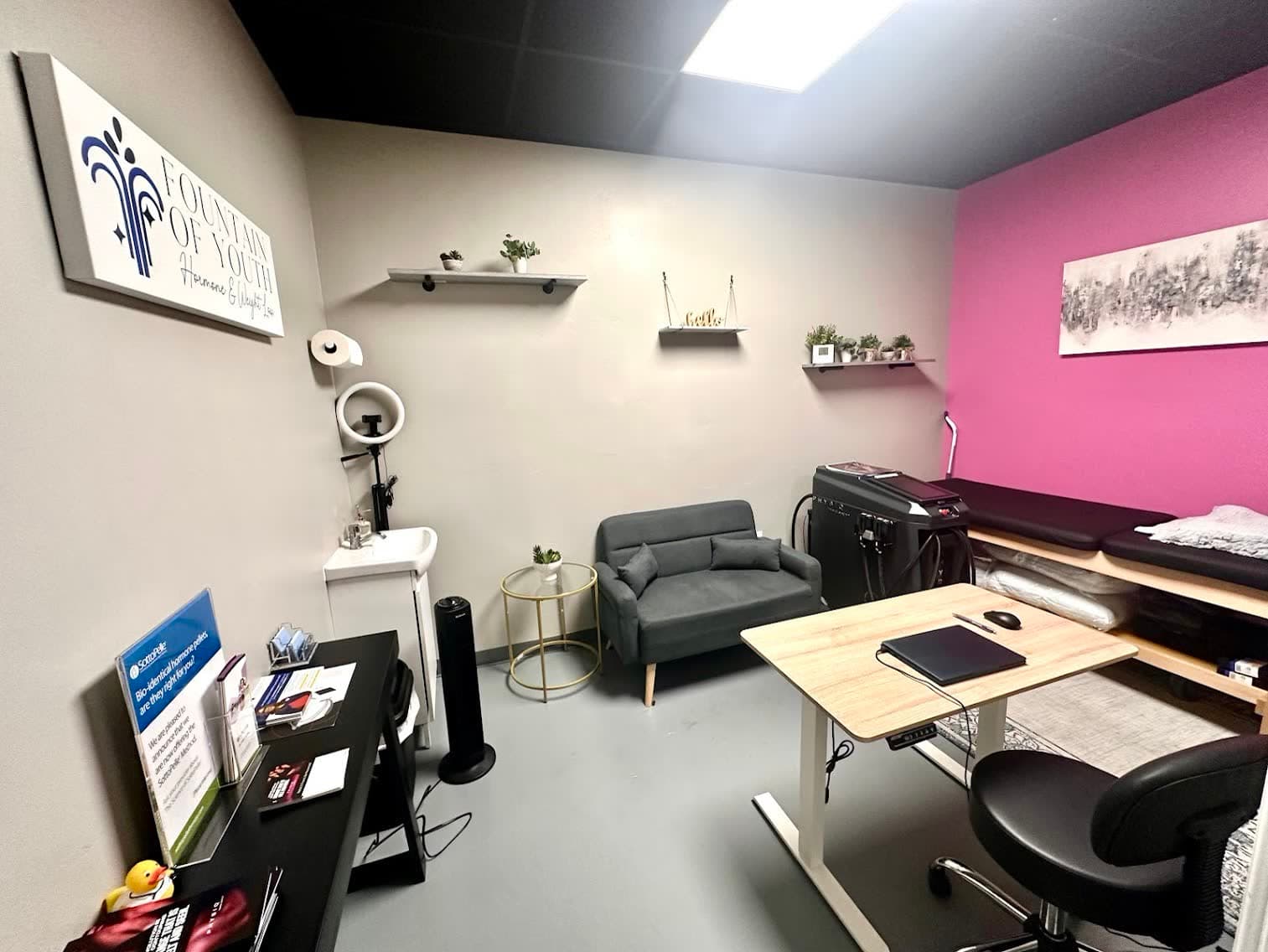 The Fountain of Youth LC consultation room in Las Cruces with the clinic logo, gray couch, and PHYSIQ 360 machine in view